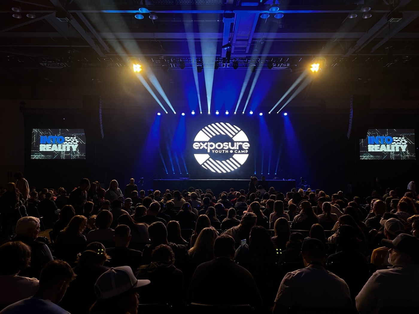 Conference audience facing a stage with LED screens and blue lighting