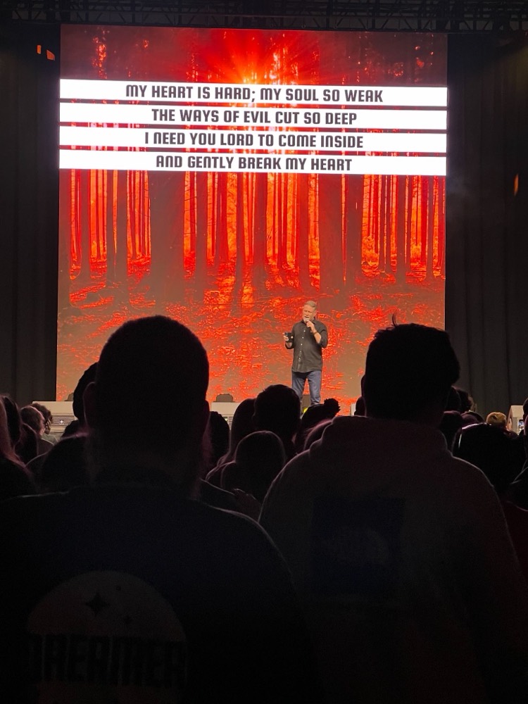 Performer on a stage washed in orange light above a silhouetted audience